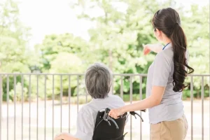 車椅子に乗る老人と介護士の女性の後ろ姿
