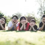 芝生の上で寝転がって幸せそうに微笑んでいる日本に滞在中の5人家族